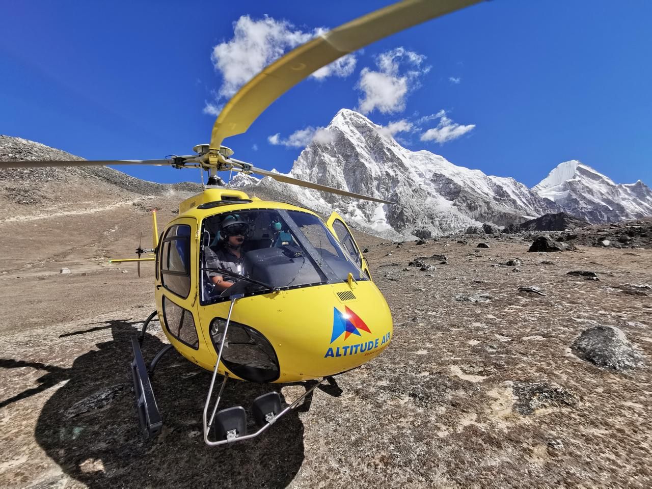 A blue helicopter sits on a snow-covered landing pad in the high Himalayas.