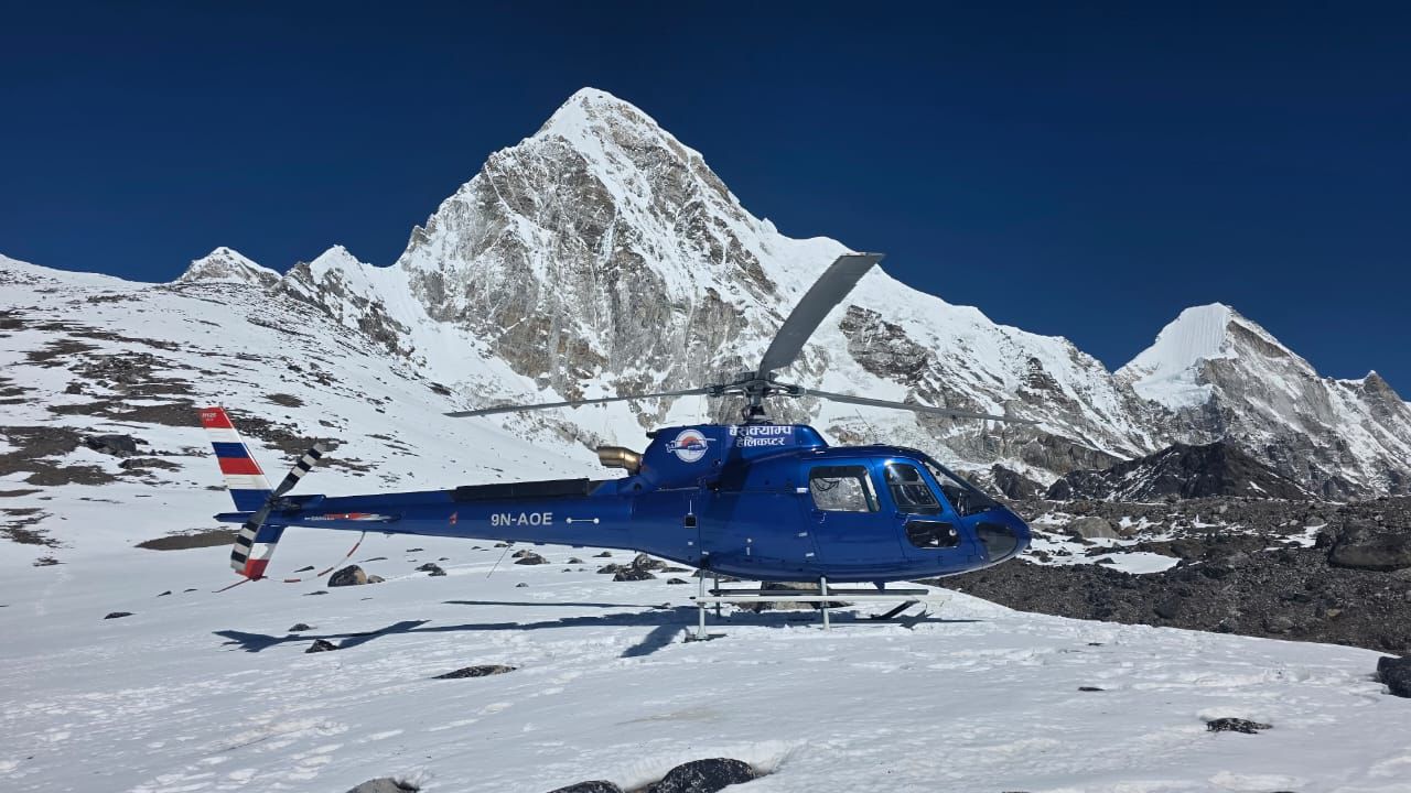 A blue helicopter sits on a snow-covered landing pad in the high Himalayas.